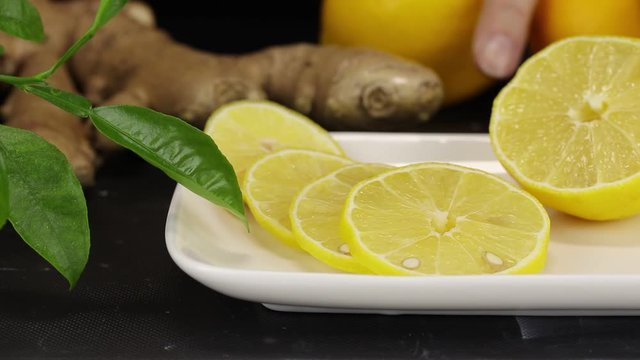 Sliced lemon slices lie in the foreground, in the background someone puts ginger root and two lemons