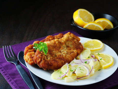 Schnitzel with potato salad served with lemon slices and parsley leaves, low-key
