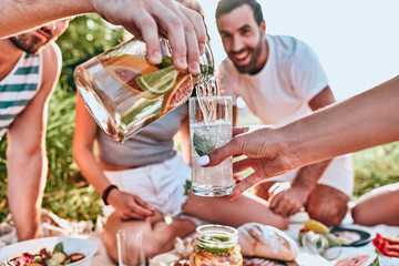 Guy pouring fresh homemade lemonade into glass of his girlfriend at outdoor party