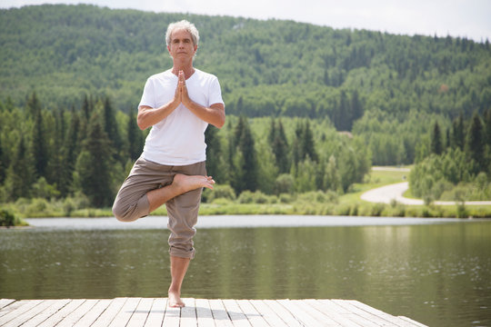 Senior man doing tree yoga pose on dock