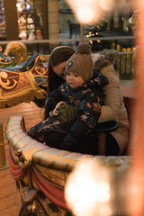 Naklejka na ściany i meble Mother and child on the carousel. Vintage carousel. The winter fair. Christmas fair. Happy family.