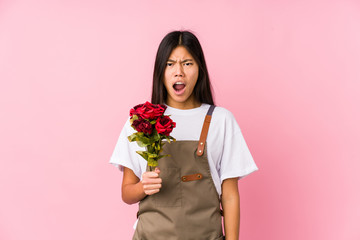 Young chinese gardener woman holding a roses isolated screaming very angry and aggressive.