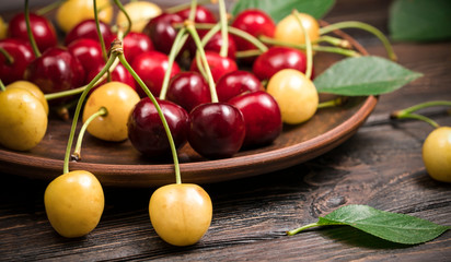 Red sweet sweet cherries in a plate on a wooden background