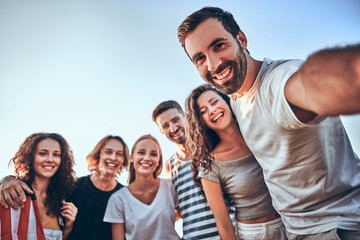 Group of happy teenage friends taking selfie on nature. Young woman with american flag background.