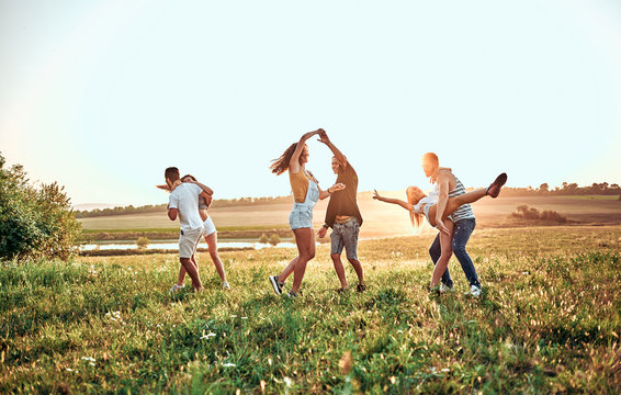 group of happy young people dancing on the field on beautiful summer sunset
