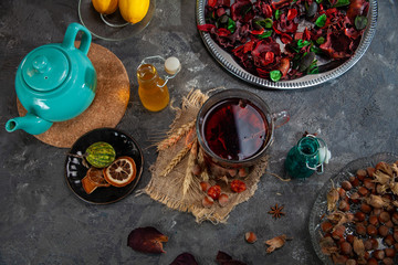 Red Hot Hibiscus tea in a glass mug on a wooden table among rose petals and dry tea custard with metallic heart