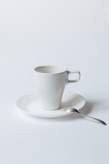 White coffee cup on a saucer and the metallic teaspoon isolated on white background
