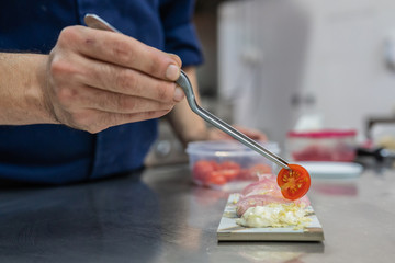 chef's hands preparing a modern kitchen dish and placing a cherry toamte over seafood salad