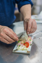 chef's hands preparing a modern kitchen dish and placing a cherry toamte over seafood salad