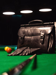 black business leather briefcase with black leather gloves on the pool table