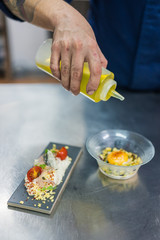 Chef hands pouring olive oil on a modern kitchen plate accompanied by a table with seafood salad next to it