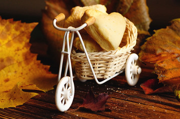A heart-shaped shortbread cookie sits on a decorative wicker cart. Around the autumn foliage, on a...