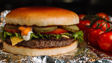 Big sandwich - hamburger burger with beef, pickles, tomato and tartar sauce on black background.