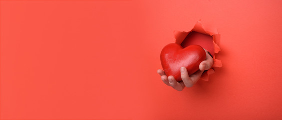 Hand holding red heart on torn red paper wall. Copy space aside for your advertising and offer or sale content. Valentines day, mother day, social advertising concept
