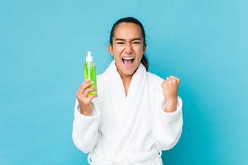 Young mixed race indian holding an aloe vera bottle cheering carefree and excited. Victory concept.