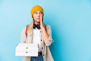 Young caucasian woman holding pizzas isolated is saying a secret hot braking news and looking aside