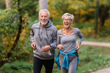 Cheerful active senior couple jogging in the park. Exercise together to stop aging. - obrazy, fototapety, plakaty