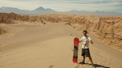 Man with sand board at a dune in the Atacama desert near San Pedro de Atacama, Chile.