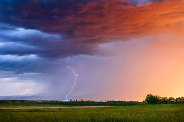 Thunderstorm lightning strike over a field at sunset