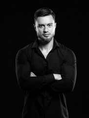 Handsome man in black shirt smiling isolated on dark background. Standing cross hands. Muscular male, athletic. Fashion portrait. Black and white
