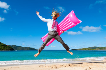 Happy businessman wearing straw hat and oversized sunglasses jumping for joy with a pink lilo on a tropical beach