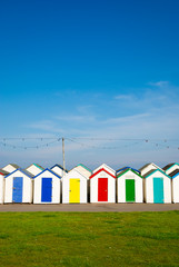 Row of colorful beach huts standing between blue sky and green grass