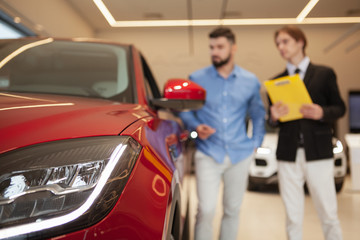 Selective focus on car lights, auto dealer and male customer talking on background at car dealership