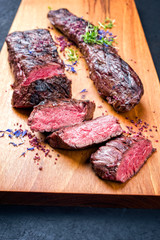 Gegrilltes dry aged Hirsch Filet Medaillon Steak natur mit Kräutern und Salz angeboten als closeup auf einem Modern Design Holz Board