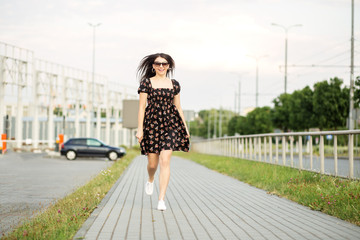 An adult smiling woman walks down the street in a stylish dress. The concept of the style of life, urban and active life.