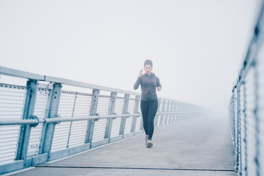 A pretty young woman brisk walking on a bridge on a misty day.