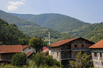 cozy rural houses among the trees and the river with visible minarets of the mosque. Architecture of residential buildings in Bosnia and Herzegovina.