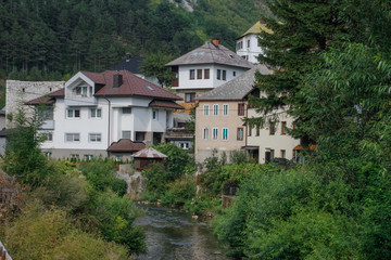 Fototapeta na wymiar rural houses among the trees and the river with visible minarets of the mosque. Architecture of residential buildings in Bosnia and Herzegovina.