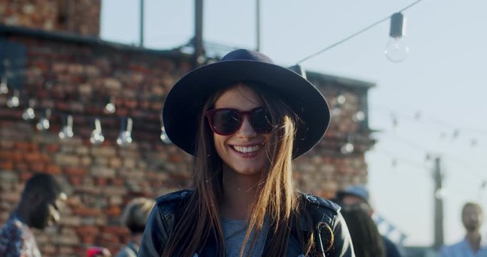 Portrait of the cute beautiful young girl in dark sunglasses and hat smiling joyfully to the camera while being outdoors. Close up.