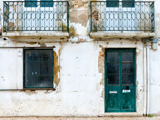 Old neglected abandoned white townhouse with green doors and metal balconies somewhere in the south...