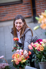 Fototapeta premium A woman holding a rose and checking out a flower arrangement basket in front of a flower shop on the street.