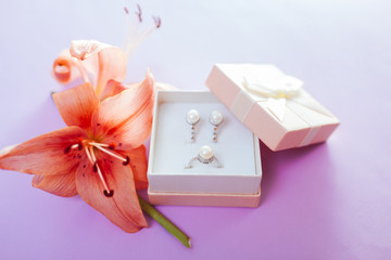 Set of pearl jewellery in the gift box with flowers. Earrings and ring with lily on purple background. Accessories