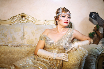 gatsby style 30s woman in shiny evening gown with a tiara on her head and long gloves. sitting on...