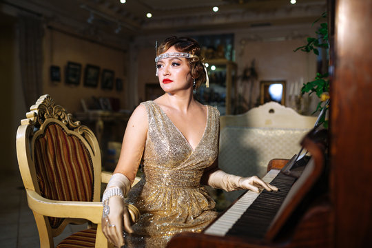 a girl in the image of 20-30 years in the style of gatsby in an evening shiny ash dress with a diadem on her head and long gloves, sitting at a pionino and looking to the side