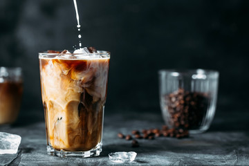 Fototapeta Milk Being Poured Into Iced Coffee on a dark table obraz