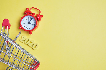 Abstract image of the year 2020 of wooden letters next to a trolley and clock on a yellow...