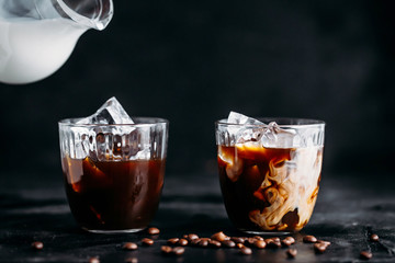 Pouring milk into a glass of espresso coffee with ice