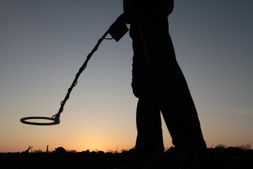 Silhouette of a man with a mine detector on the background of the setting sun