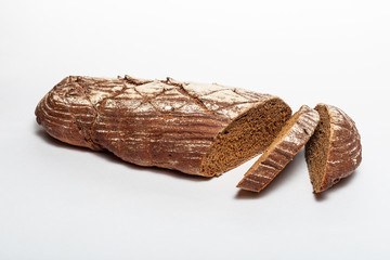 Sliced loaf of black rye bread with cuts from a knife on top of it and sprinkled with white flour isolated on a white background. Healthy eating concept.