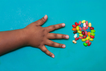 A kids arm and hand with fingers spread out that is about to grab fruit flavored candy from a small serving.