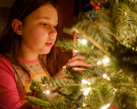Pretty young girl in pajamas looking at a Christmas tree and dreaming .