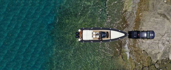 Aerial top view ultra wide photo of inflatable speed boat on trailer being towed by truck from emerald exotic sea to land - Powered by Adobe