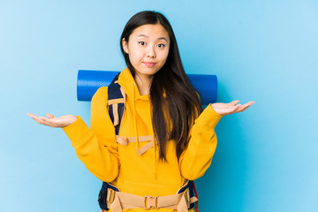 Young chinese backpacker woman isolated doubting and shrugging shoulders in questioning gesture.