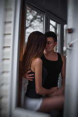 Fototapeta na wymiar A loving young couple hugs in the window of their balcony terrace in the apartment. Young man laughs with a beautiful woman at home. Lovers kiss, passionately spend time with each other. Lifestyle
