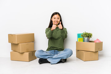 Young chinese woman moving to a new home with thumbs ups, cheers about something, support and...