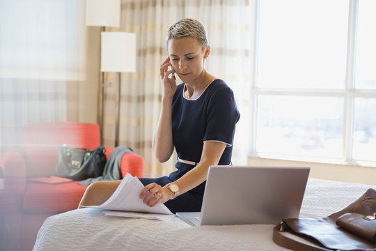 Businesswoman using smart phone while reviewing documents in hotel room